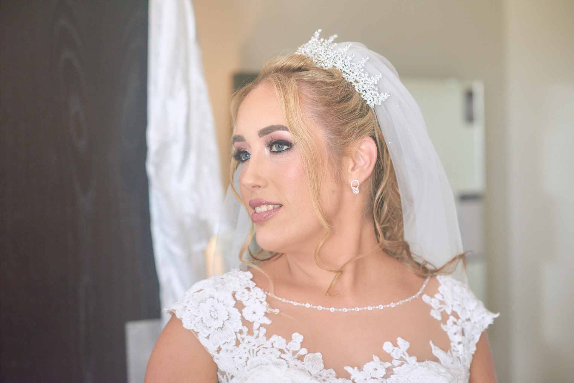 Side profile of bride dressed up in her wedding dress and just after getting her make up done in the hotel room. The light and the background give the image a nice gentle look