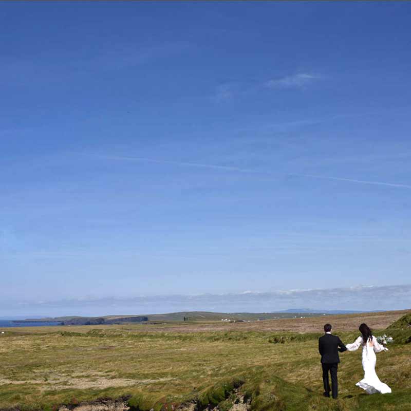 Bride and groom walk on an empty coastline dressed in their wedding clothes