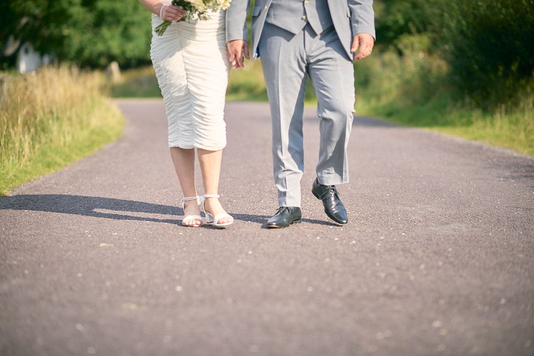 Black and white shot of a bride and groom walking toward the camera on a big gravel path. They are holding hands, deep in conversation. Background is covered in thick trees