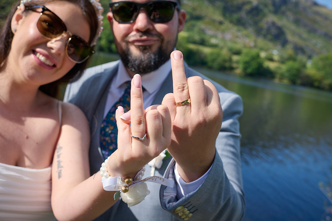 Bride and groom show off their wedding rings beside a lake