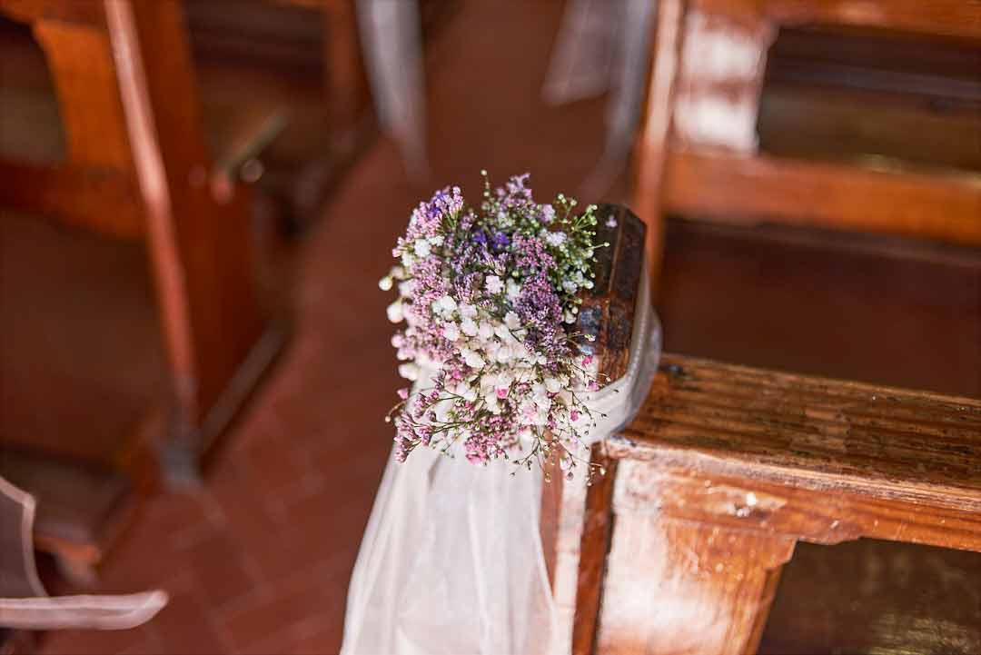 small purple and white wedding bouquet on a church pew